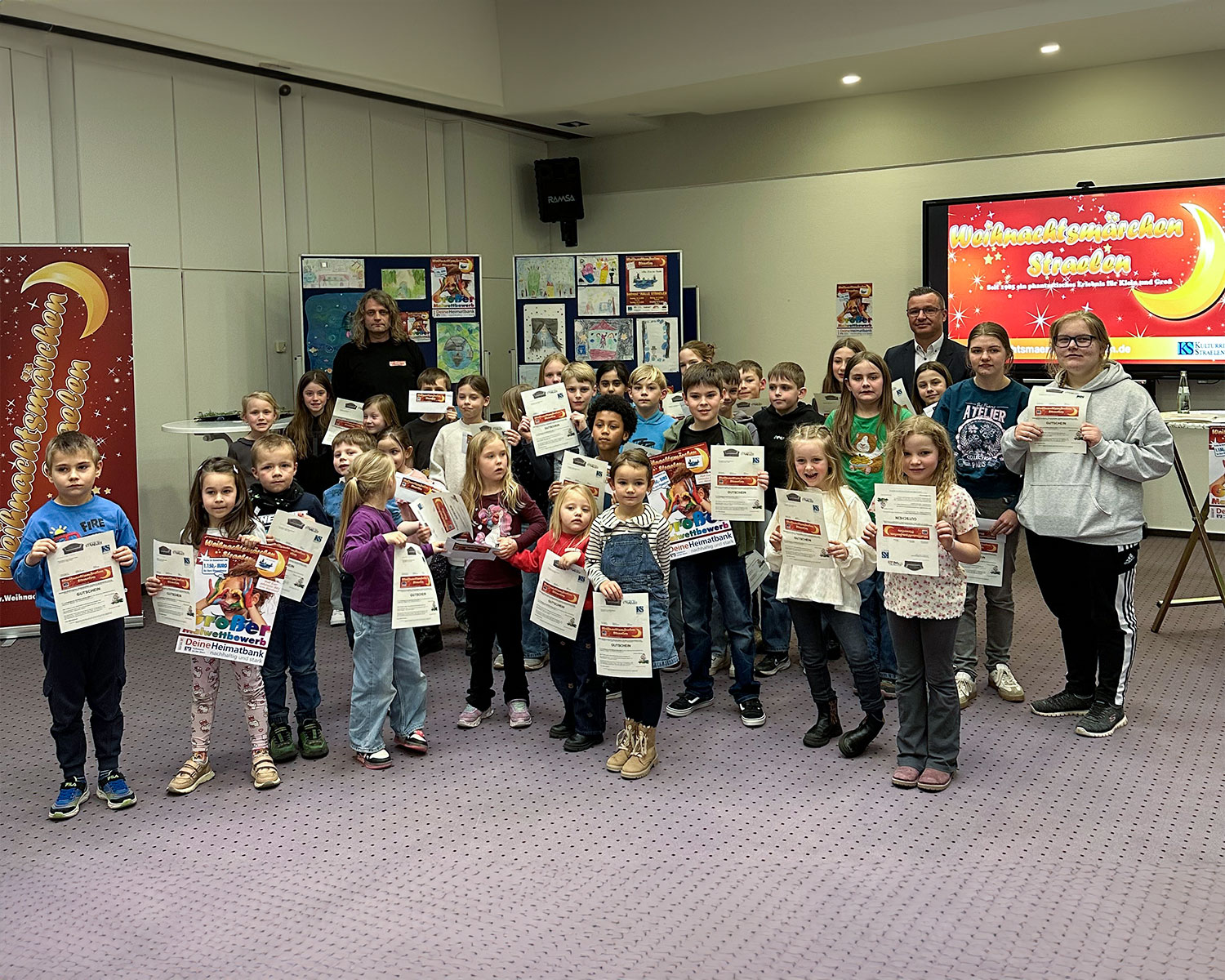 Mario Lüfkens (hi.re.), von der Volksbank an der Niers, und Norbert Kamphuis (hi.li.) vom Weihnachtsmärchen Straelen verteilten Geldpreise im Gesamtwert von 1.150,00€ an die stolzen Gewinnerinnen und Gewinner des 15. Voba-Malwettbewerbs zum letzten Weihnachtsmärchen „Wasser des Lebens“ aus 2025.